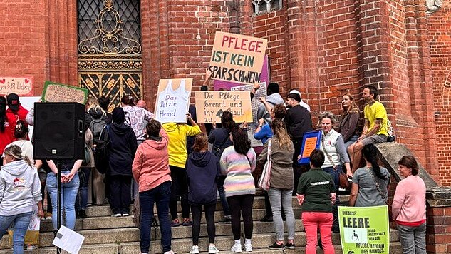 Menschen protestieren mit Schildern für bessere Pflege vor einer Backsteinkirche in Frankfurt/Oder