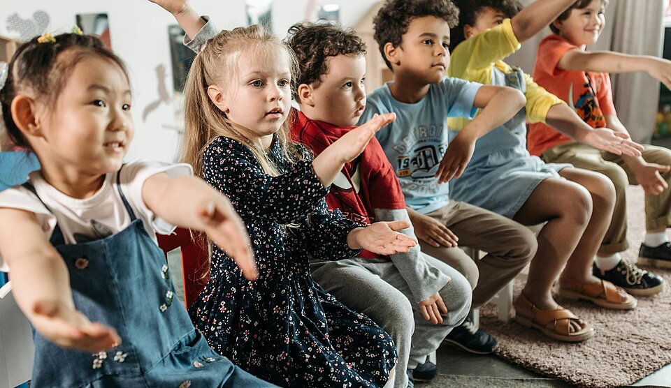 Kinder machen Bewegungsübung im Sitzkreis