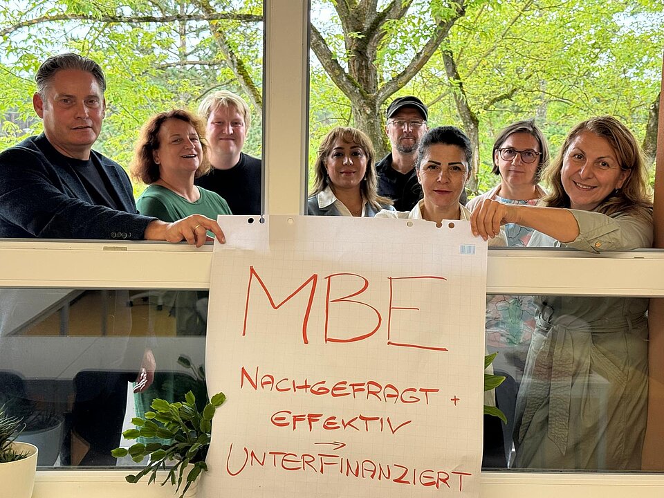 Gruppe hinter Plakat „MBE unterfinanziert“