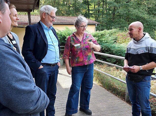 Gruppe von fünf Personen im Gespräch vor einem Gebäude am Waldrand.