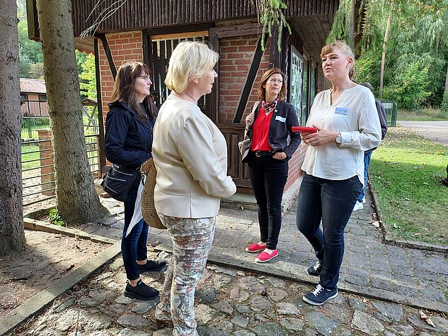 Vier Frauen unterhalten sich vor einem Fachwerkhaus im Grünen.