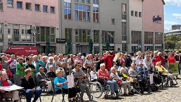 Große Versammlung auf einem Stadtplatz, viele sitzend, teils mit Rollstühlen