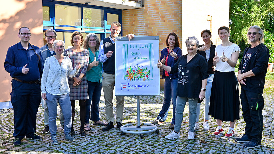 Gruppe vor Gebäude mit Willkommensschild