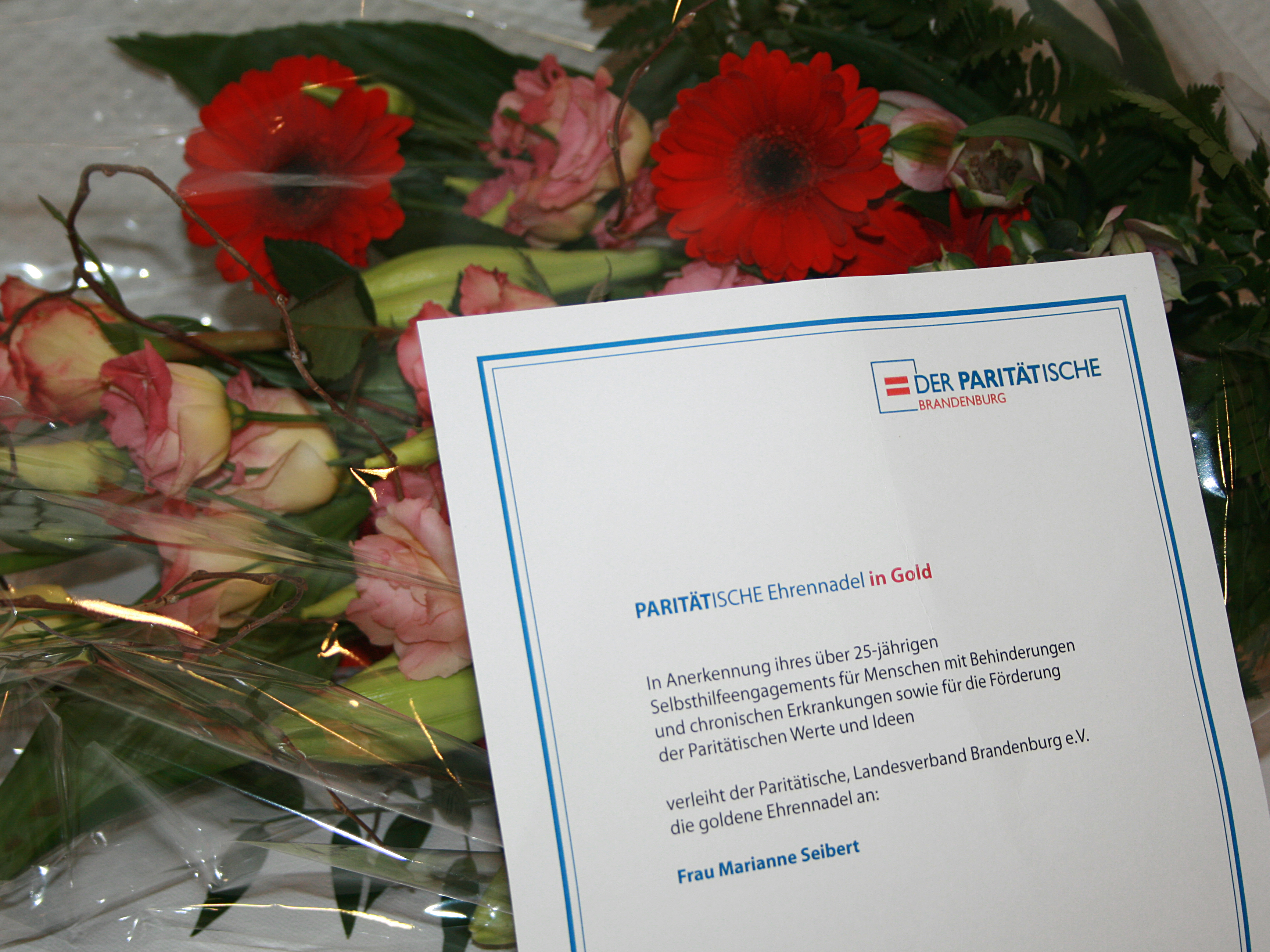 Paritätische Ehrennadel in Gold, Urkunde und Blumen